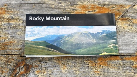 A Rocky Mountain National Park Map is sitting on a wooden bench