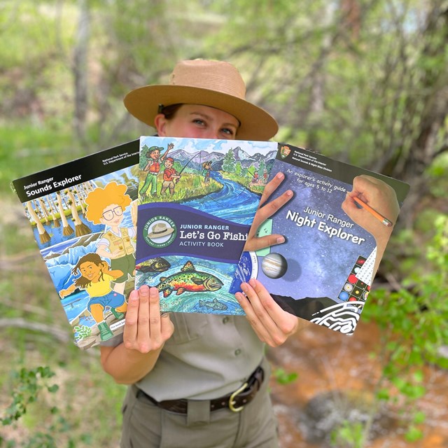 A Park Ranger is hold three different Junior Ranger Explorer books