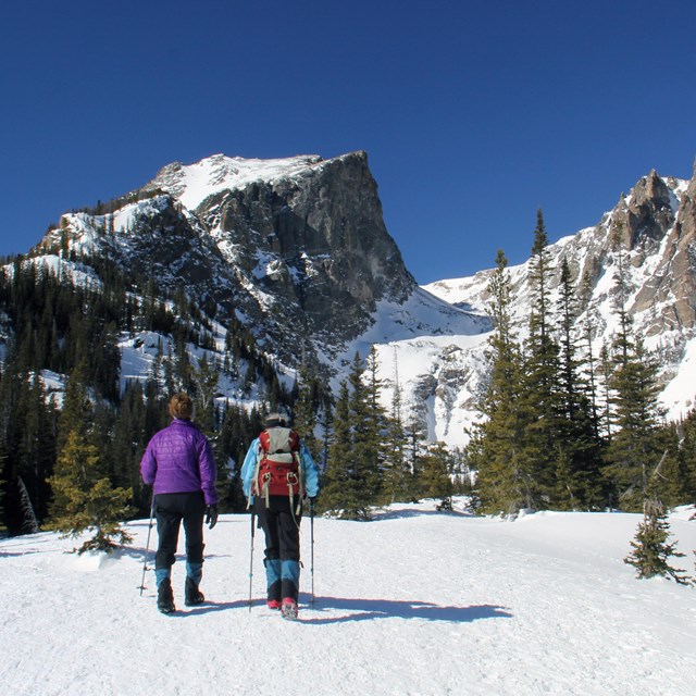 Two people are hiking in the snow using traction devices
