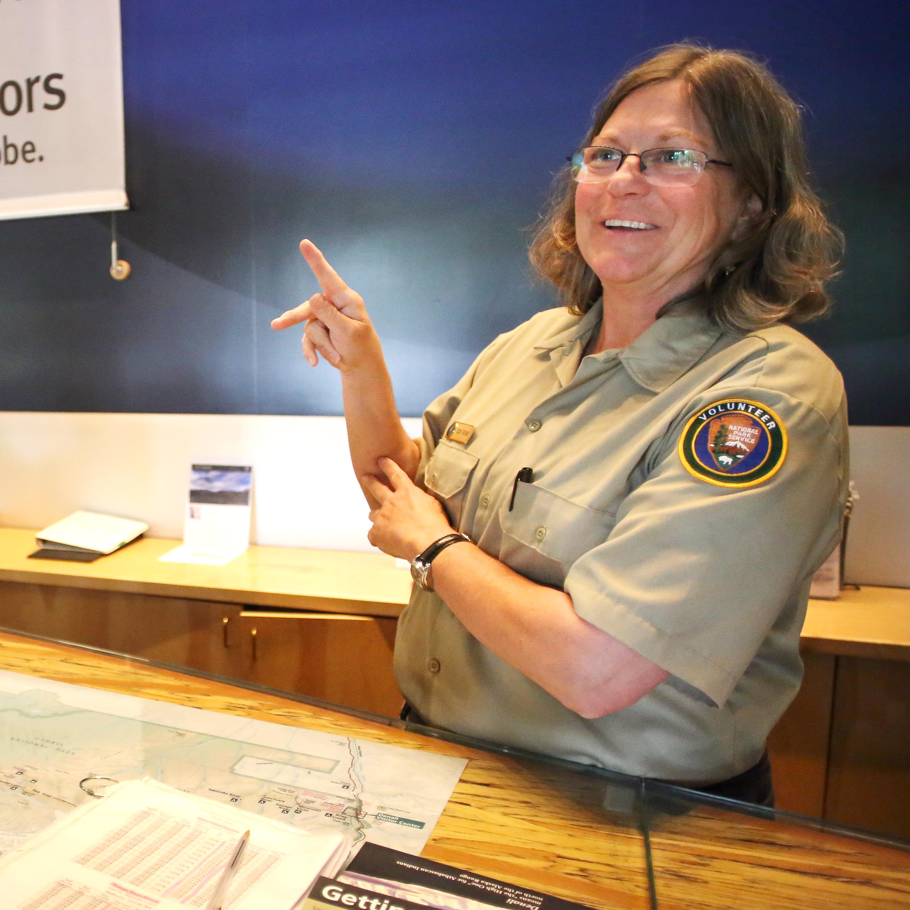 A person wearing a volunteer uniform signs in ASL with a Deaf visitor.