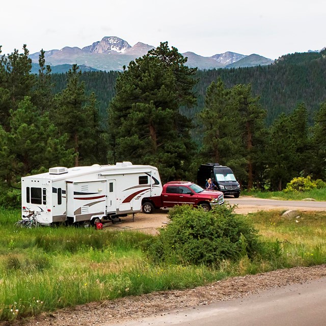 Three RV-campsites with picnic tables are seen in a grassy area