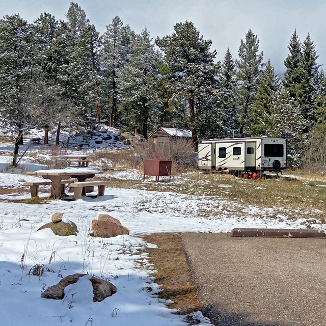 A view of a campsite in Aspenglen Campground with an RV parked. The campsite has snow on the ground