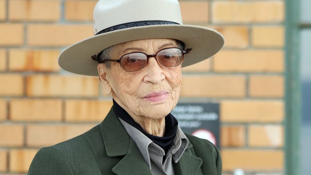 Older African American woman in ranger uniform sits on concrete porch.