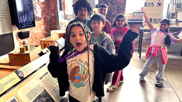 A group of children happily smile and pose in front of the visitor center exhibit.
