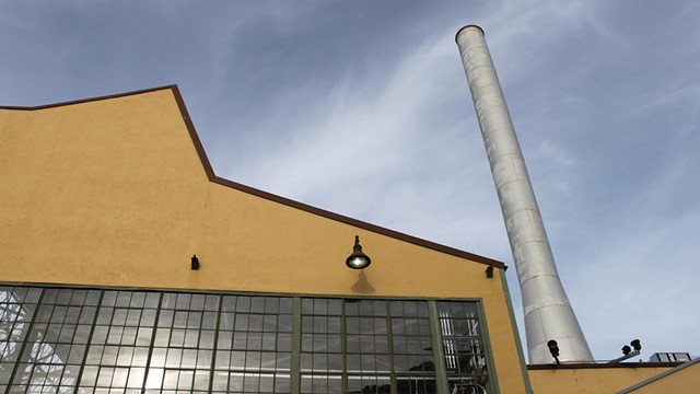 Cropped photo of part of the Ford Assembly building. Windows and a tall stack. 