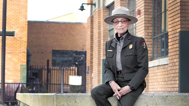 Older African American female ranger sits on concrete porch. 
