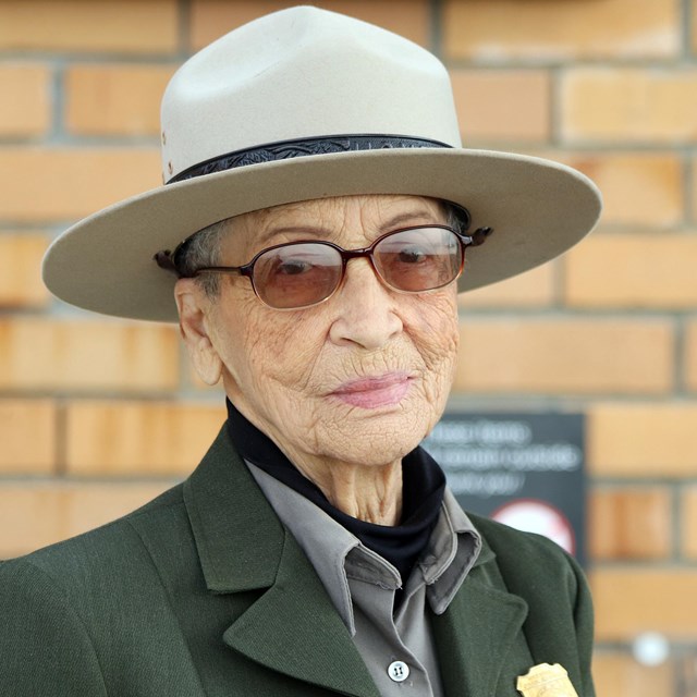 Older African American woman in ranger uniform sits on concrete porch.