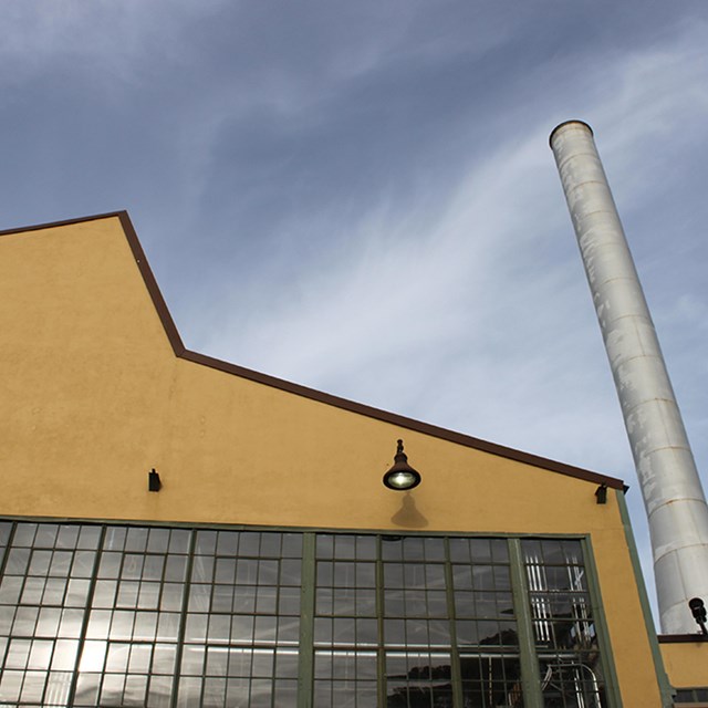 Cropped photo of part of the Ford Assembly building. Windows and a tall stack. 