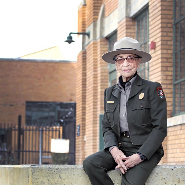 Older African American female ranger sits on concrete porch. 