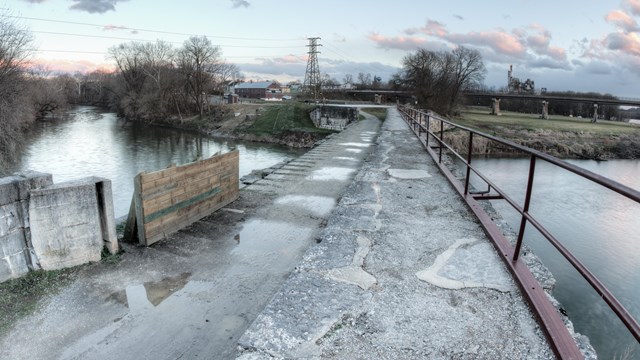 An abandoned bridge crosses over a river under a cloudy grey sky.