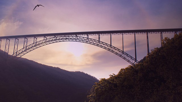 A bridge in front of a sunset over a river