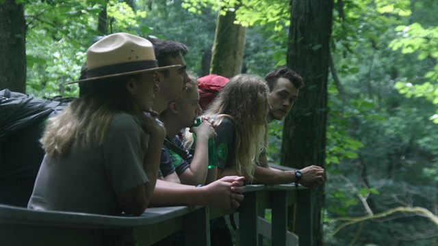 A ranger looks over the boardwalk railing with visitors.