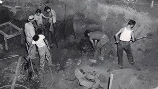 Several men working in pit within cave shelter