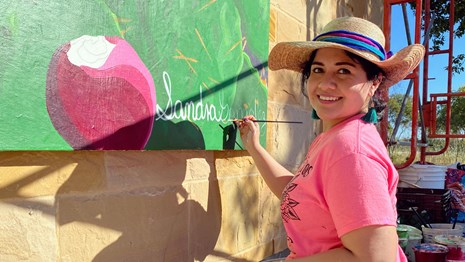 Artist Sandra Gonzalez signing her name on the Tricentennial Mural at the Visitor Center.