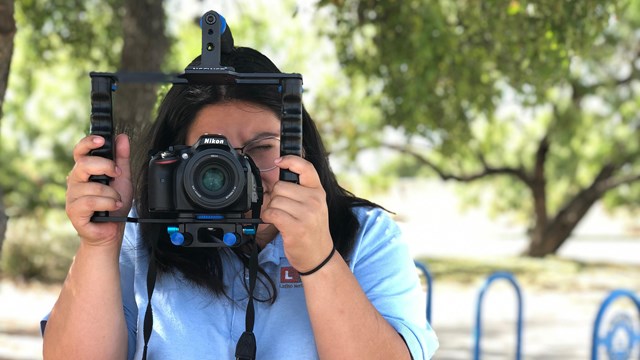 Latino Heritage Intern holding a camera up to her face.