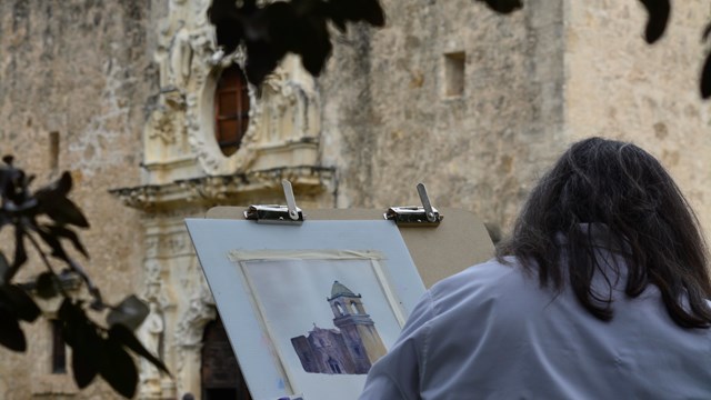 Woman paints the Mission San José facade.