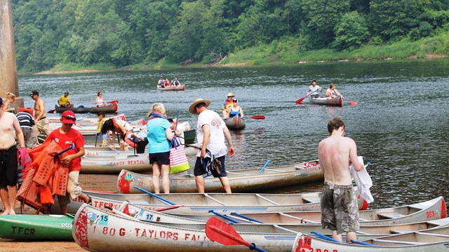 People standing by and getting out of canoes on sandy beach landing.
