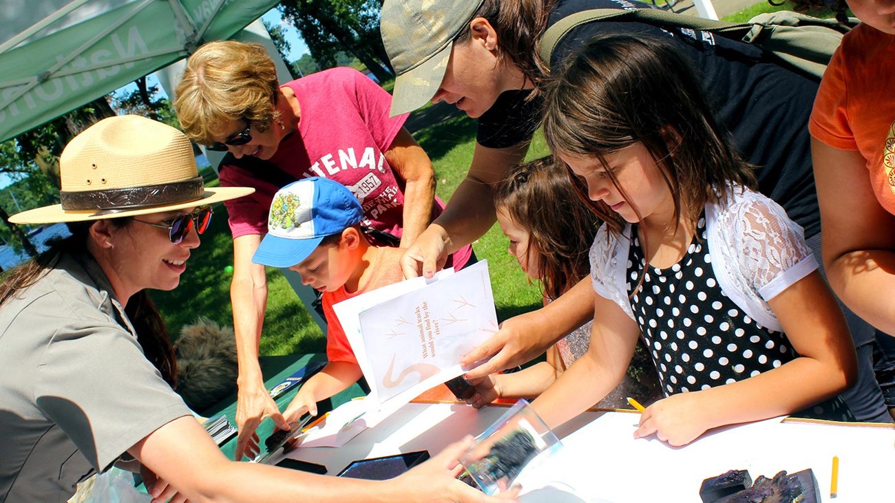 Park ranger shows kids and adults animal track stamps at a table.