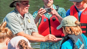 Park ranger shows something in hand to group of people wearing life jackets