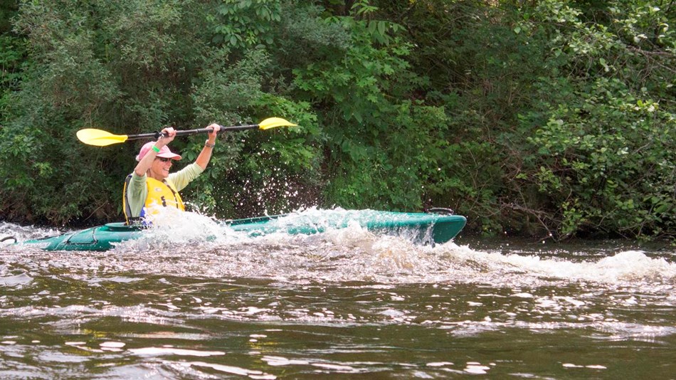 A kayaker paddles through waves with her paddle raised.