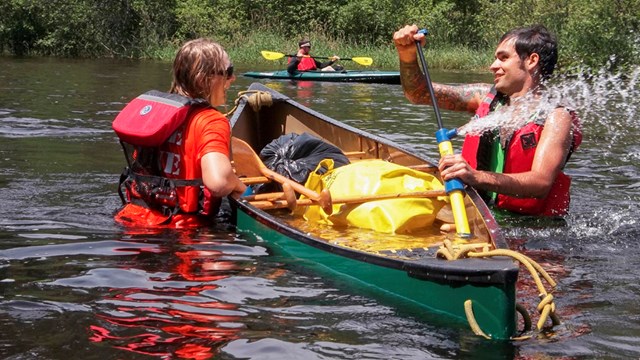 Two paddlers stand in river next to swamped canoe pumping out water