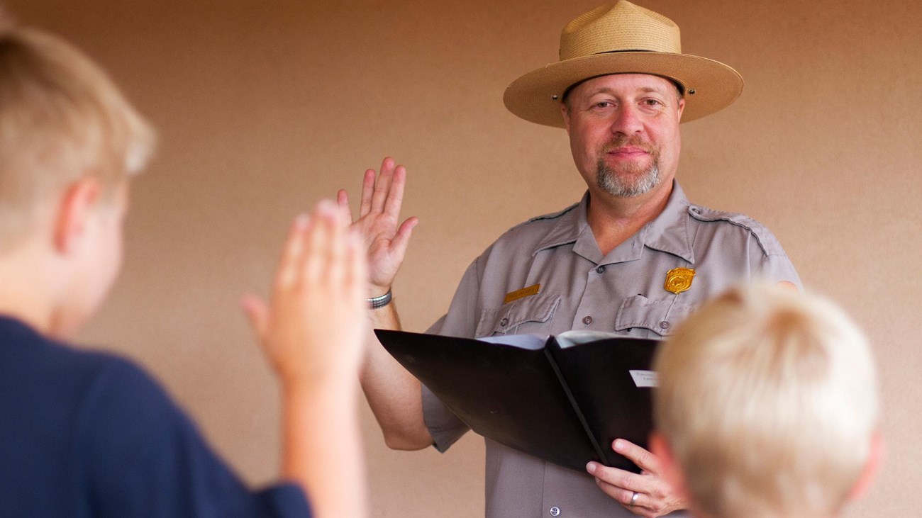 A ranger in a flat hat swears in two young boys.