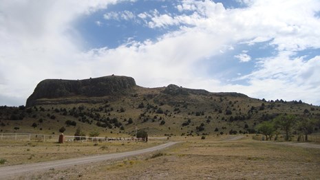 grassy foreground, road leading to verdant green mountain, white clouds above