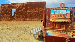 Art easel with a painting-in-progress in front of an adobe ruin