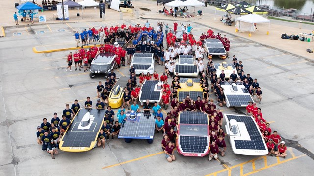 Solar cars with their teams in matching uniforms.