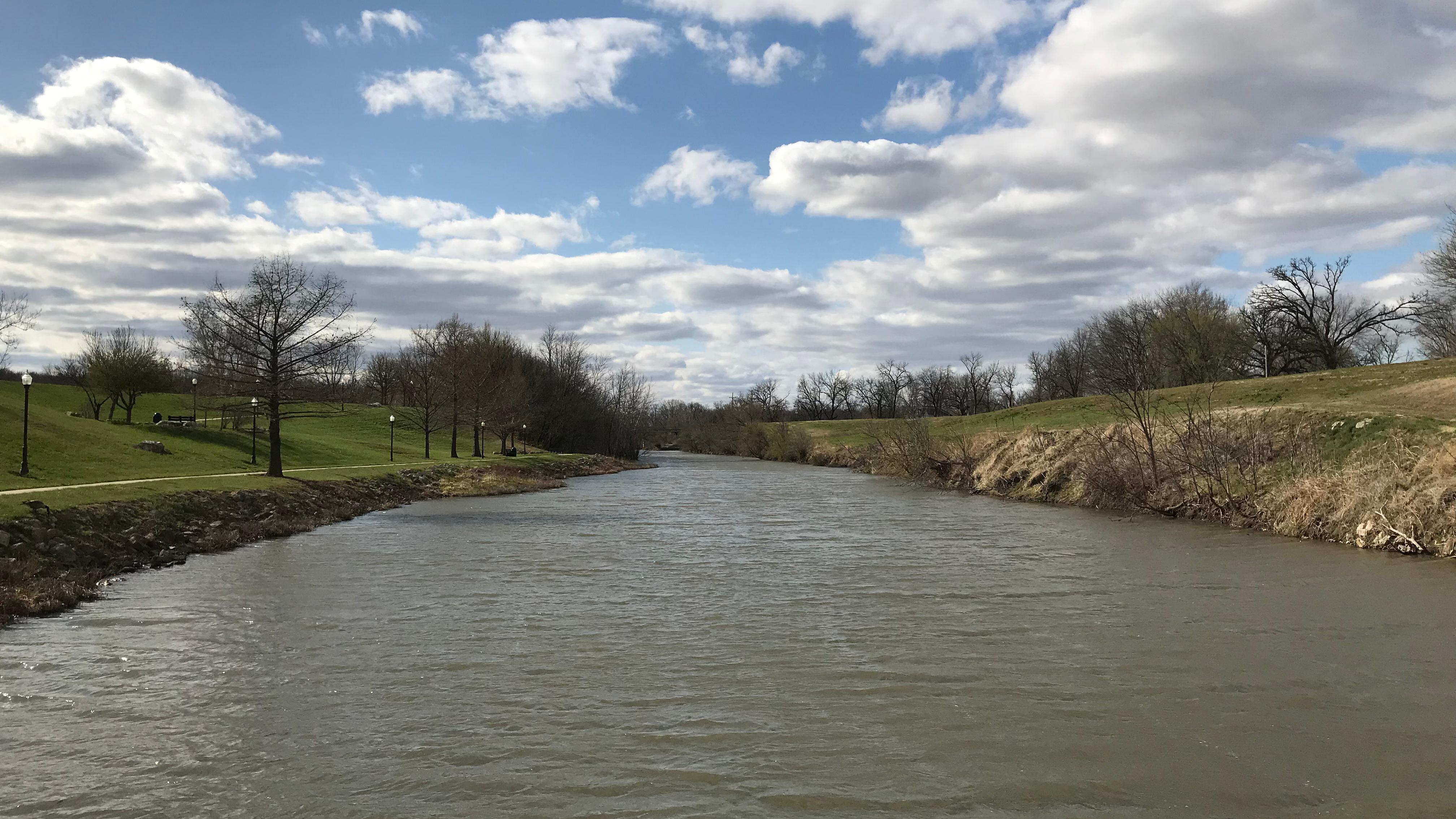Looking down a wide muddy river, with vegetation on the banks, under a blue sky.