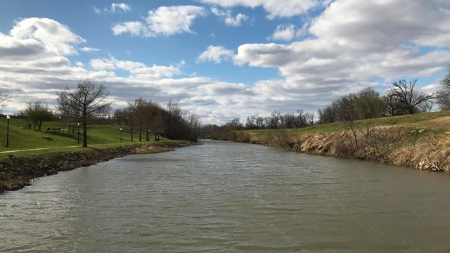 Looking down a wide muddy river, with vegetation on the banks, under a blue sky.