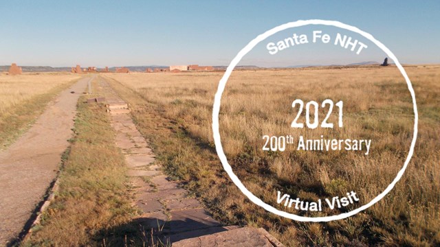 A path leads to distant adobe ruins in a flat landscape.