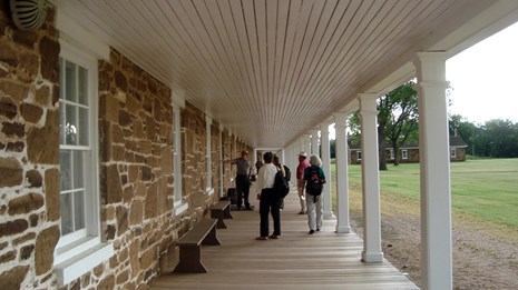 people on a porch, building with white pillars and rock walls