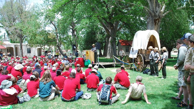 Kids and adults sit around in a circle in a grassy area.