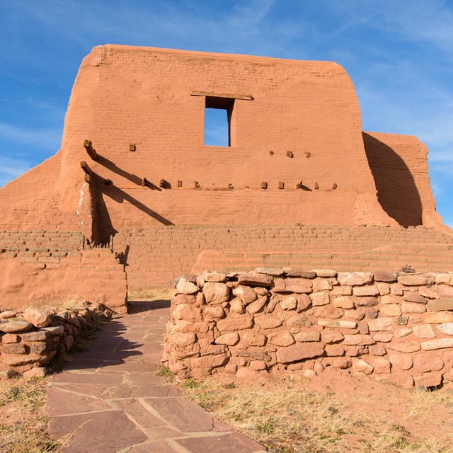 A large adobe historic church, with an adobe brick wall.