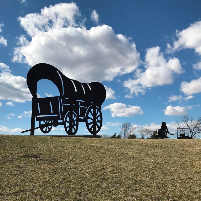 A covered wagon statue on a grassy hill.