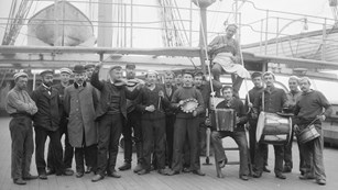 Group of men standing on the deck of a sailing ship holding various instruments