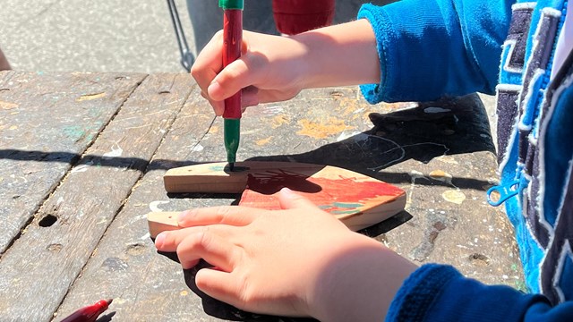 Close-up of a child's hands as a child uses a marker to color a piece of wood.