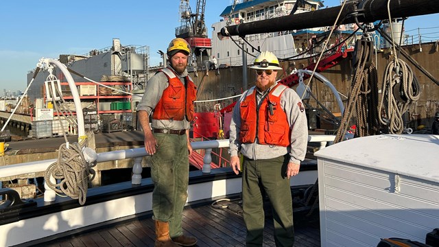 Two rangers with rigging gear stand on the deck of a ship.