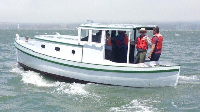 A motor vessel on the water, painted blue and white, with two men standing at the rear