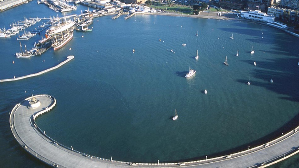 Aerial view of a long curved pier enclosing a blue water cove