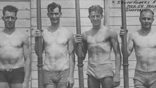 Four men in old fashioned swimming outfits standing in a row