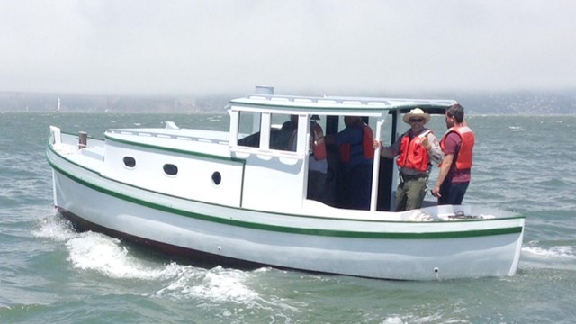 A motor vessel on the water, painted blue and white, with two men standing at the rear