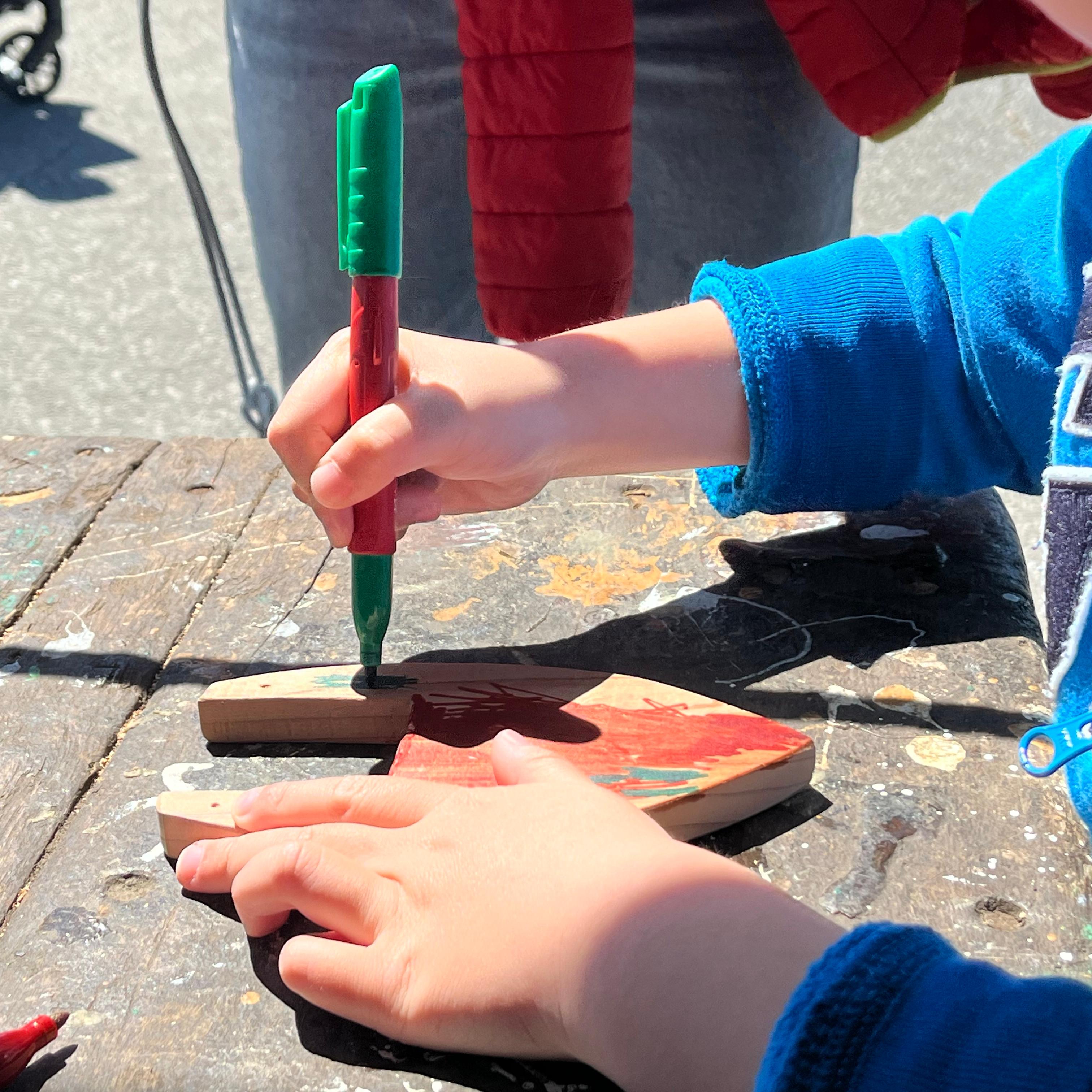 Close-up of a child's hands as a child uses a marker to color a piece of wood.