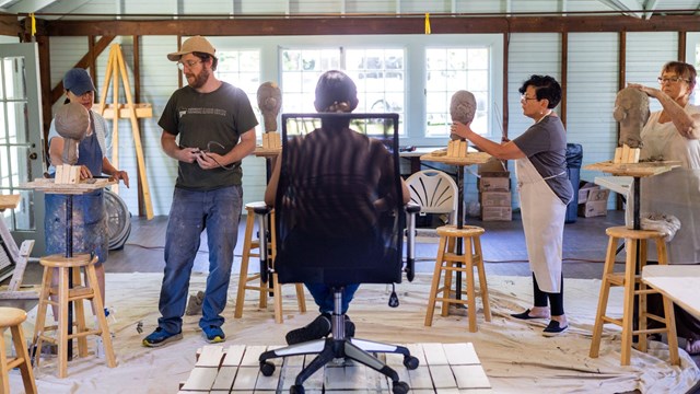 students sculpt clay busts standing around seated model