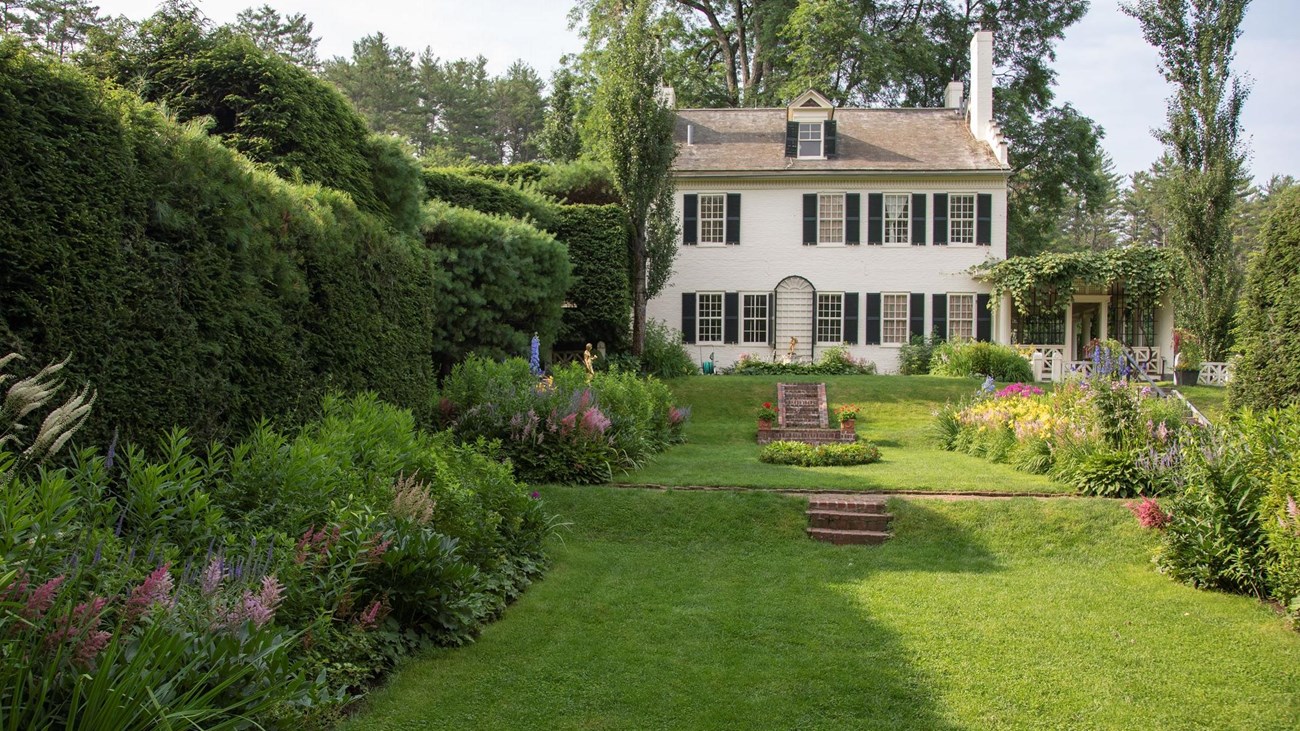 flower gardens leading to white brick house