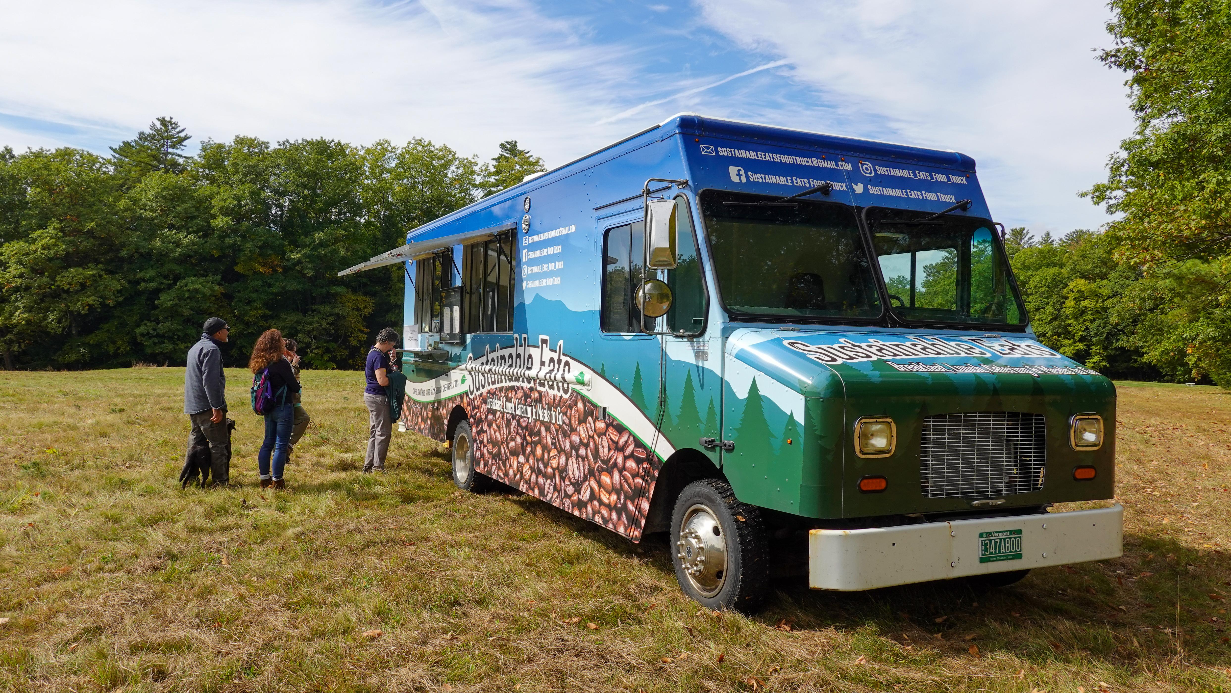 food truck in an open field with group of people waiting in line
