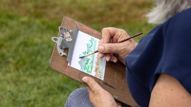 Woman sits on bench while painting with watercolors