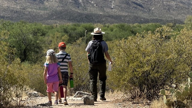 Ranger walking on a trail with two children