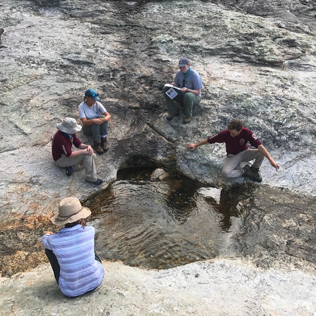 group of young people gather around desert pool surrounded by stone